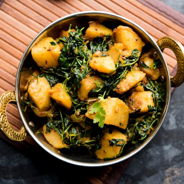A metal bowl filled with golden potato chunks and green leafy vegetables, garnished with cilantro.
